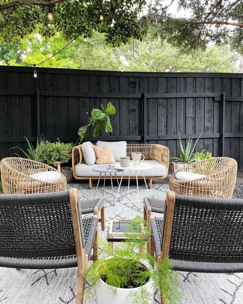 Contemporary outdoor patio with rattan furniture white cushions and black fence backdrop