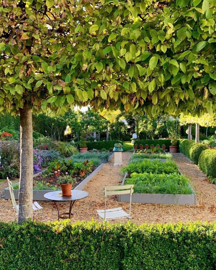 Formal garden with metal beds and bistro seating under tree
