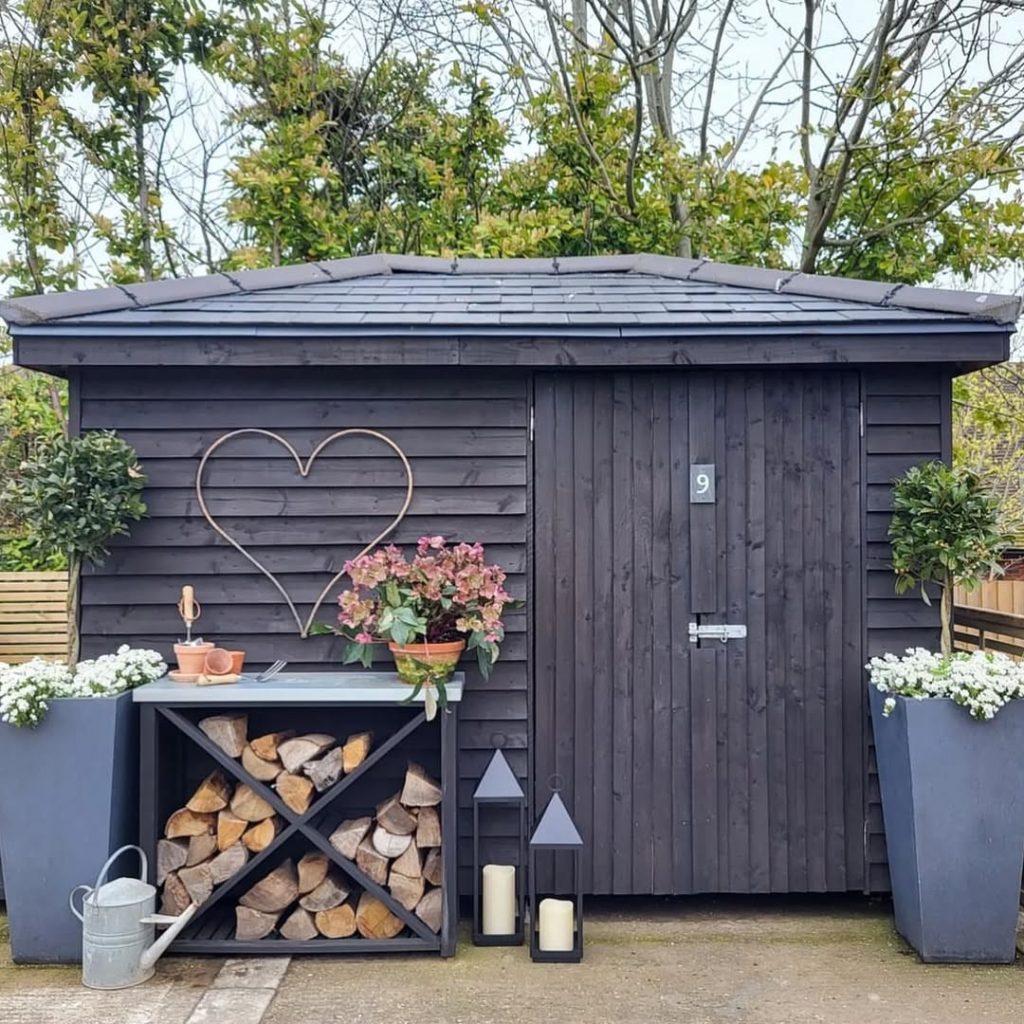 Black garden shed with heart decoration planters and firewood storage