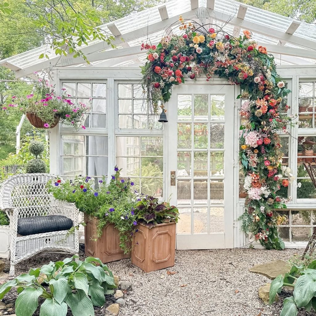 White greenhouse with floral arch wicker chair and planters