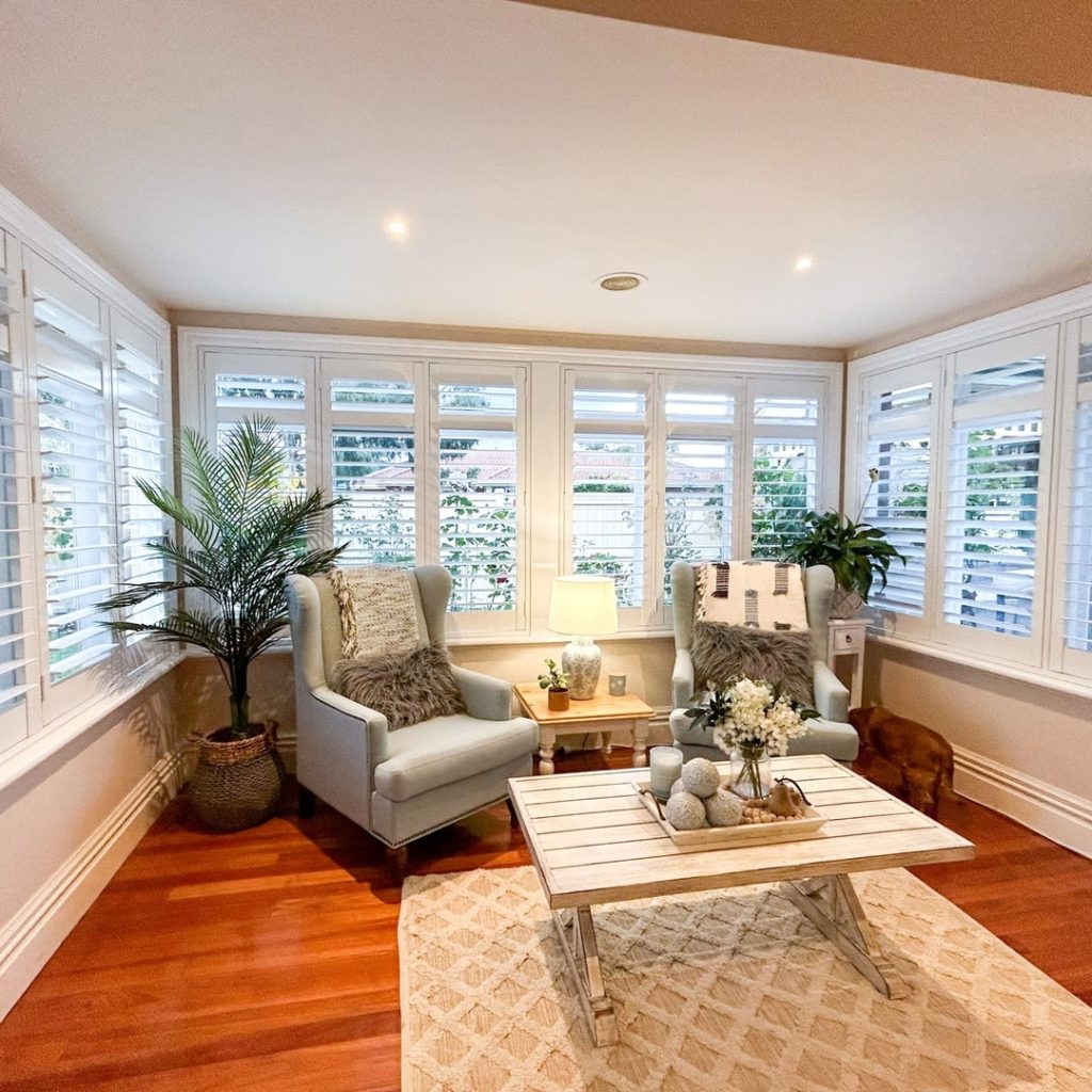Bright sunroom with white shutters gray chairs and hardwood floors
