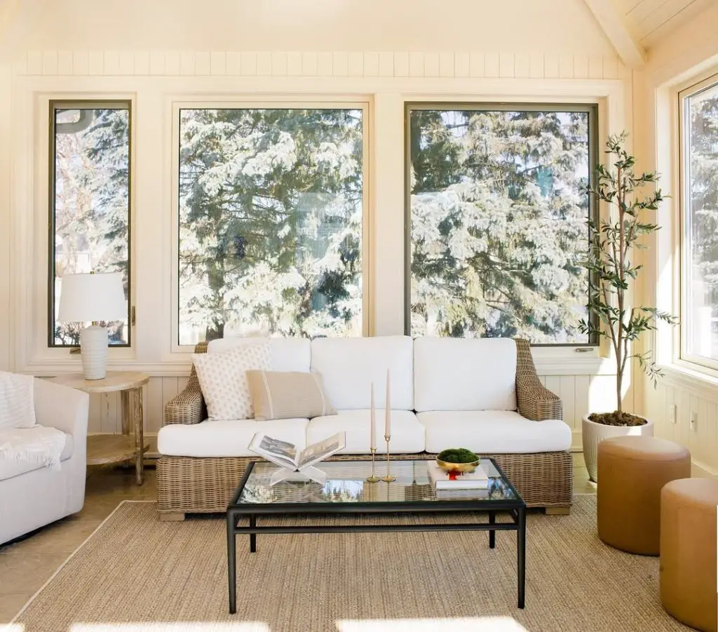 Bright sunroom with rattan furniture white cushions and snowy pine views
