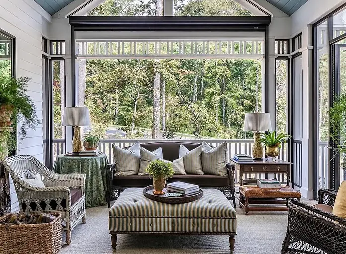 Screened porch with wicker furniture striped ottoman and forest views