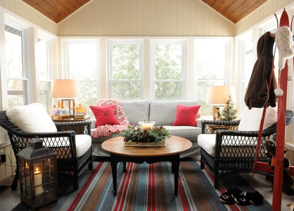 Bright sunroom with wicker furniture striped rugs red pillow