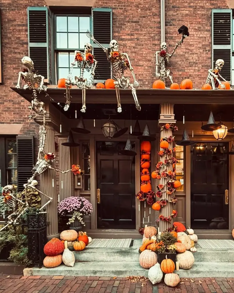 Skeletons celebrating on brick house balcony with orange pumpkins