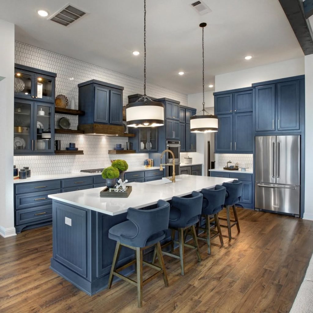 Navy blue kitchen with white hexagonal backsplash, matching bar stools, drum pendant lights