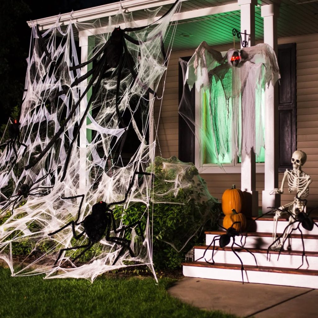 Halloween decorated front porch with spider webs, skeleton, ghost, and green lighting