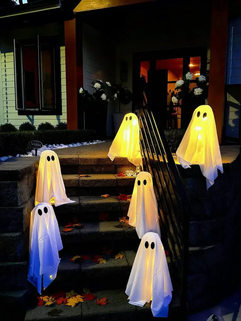 Illuminated white sheet ghosts arranged on front steps with yellow lighting