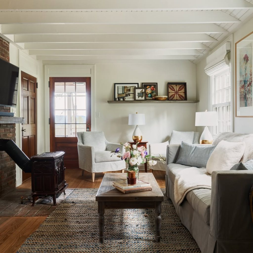 Cottage living room with white beams, gray sofa, brick fireplace, and cozy textiles
