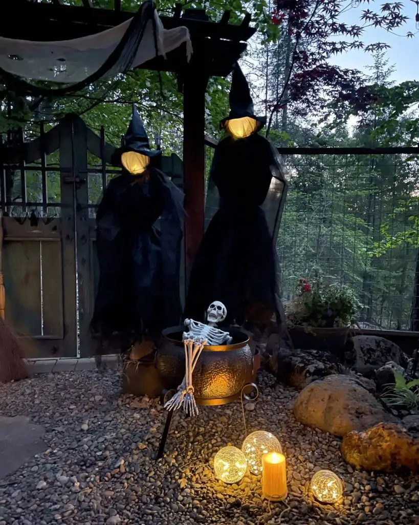 Two witch figures with glowing cauldron and skeleton in backyard setting