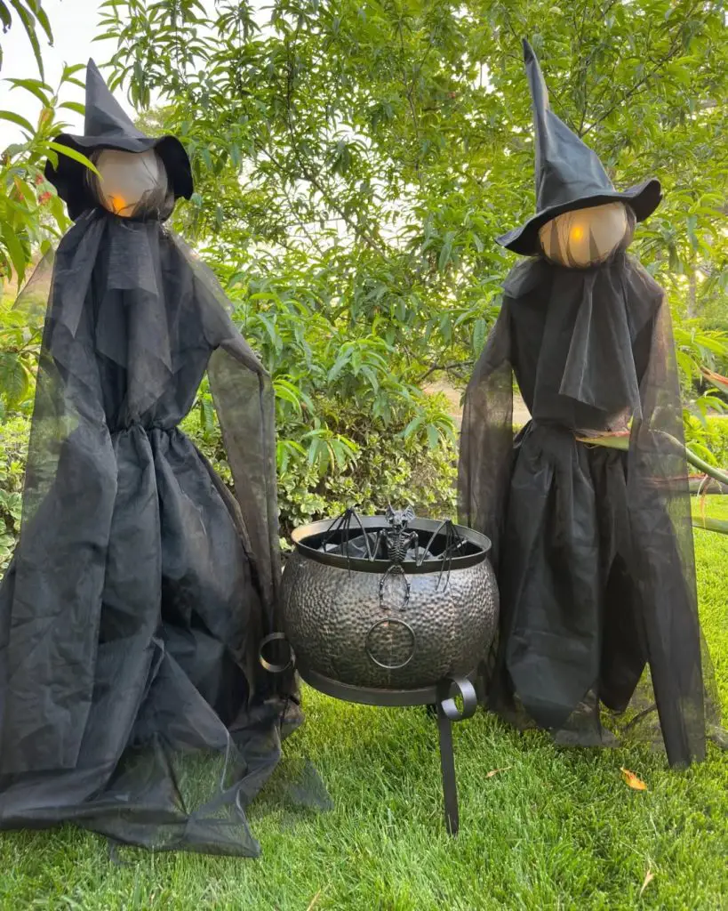 Two garden witch decorations with glowing faces surrounding decorative cauldron