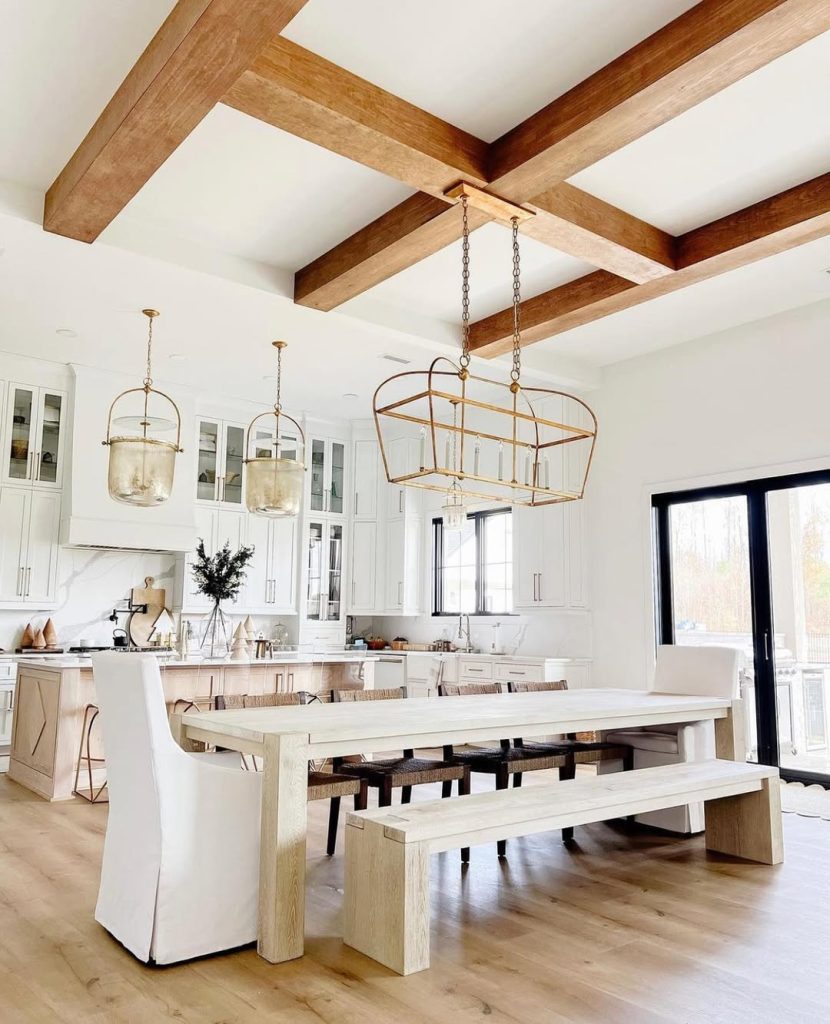 Rustic kitchen with exposed wood beams, white cabinets, brass pendant lights, farmhouse table