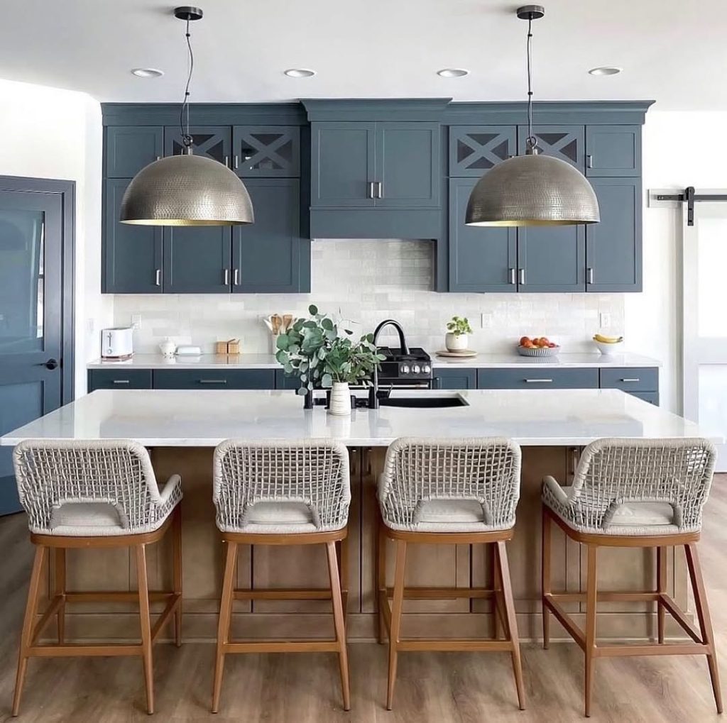 Coastal kitchen with blue cabinets, wicker bar stools, hammered metal pendant lights, white countertops