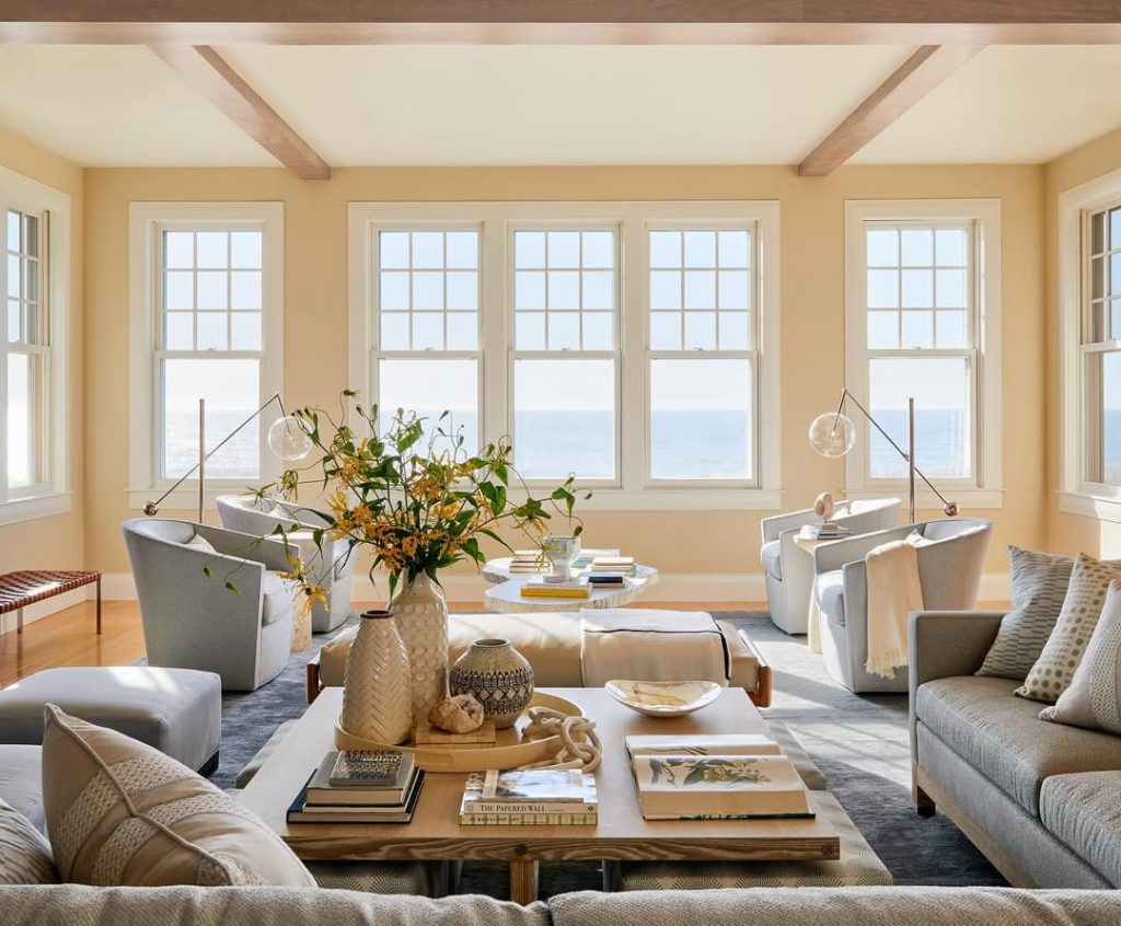 Bright living room with large windows, gray sectional sofa, brass sconces, and water views