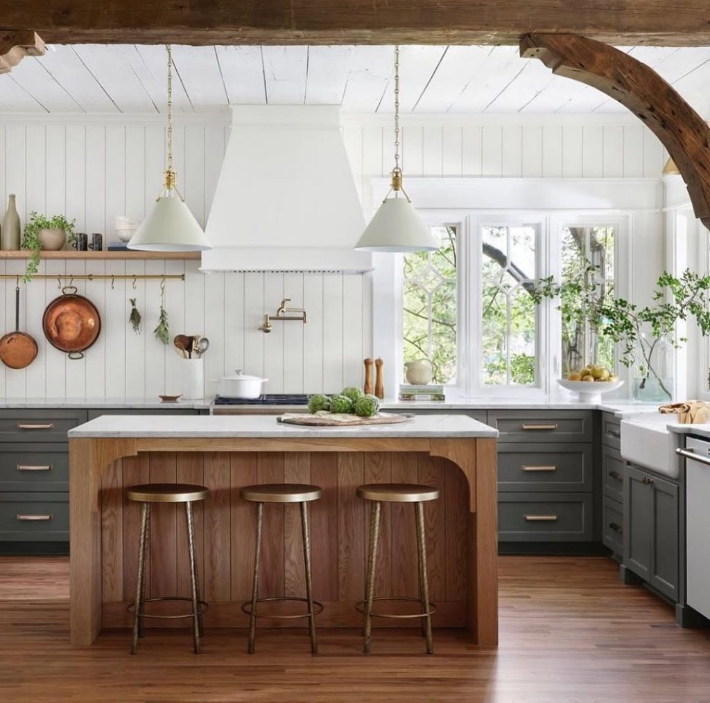 Rustic farmhouse kitchen with wooden arch, white shiplap walls, copper cookware, sage cabinets