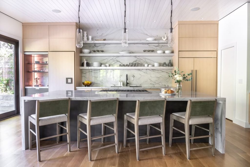 Bright kitchen with marble backsplash, wooden bar stools, floating shelves, pendant lighting