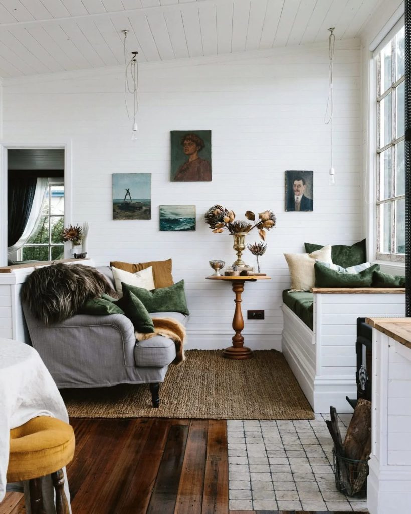 Cozy living room with white walls, dark wood floors, green velvet pillows, and vintage paintings