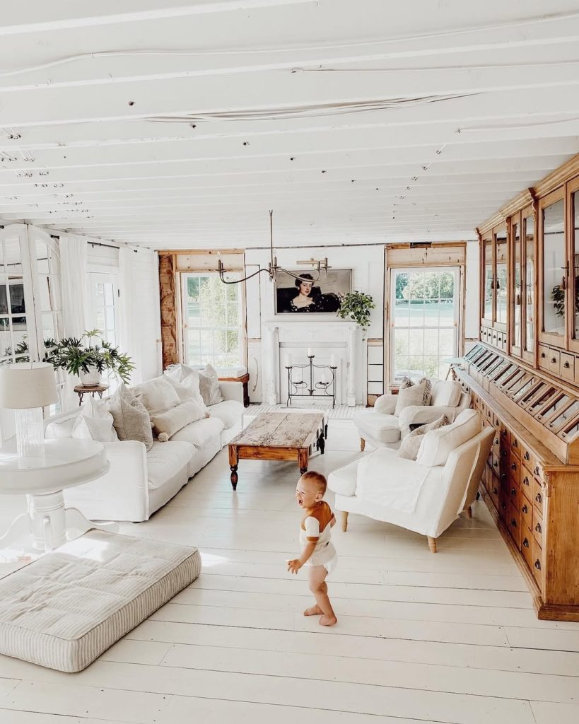 White living room with built-in storage, neutral furniture, large windows, and a child playing on wooden floors