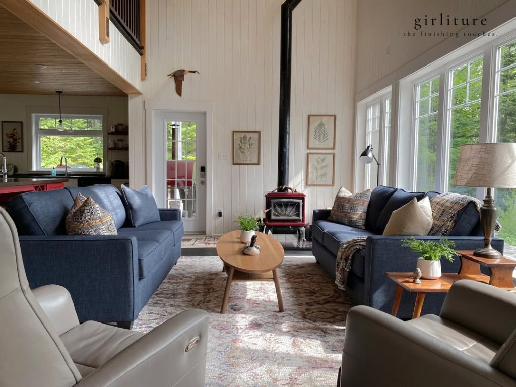 Modern cabin living room with navy sofas, white wood panels, stone fireplace, and large windows