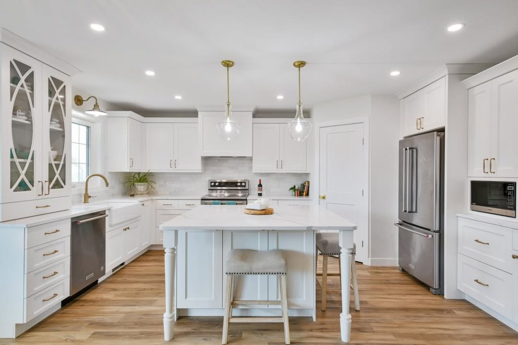 Farmhouse kitchen with glass pendants, white cabinets, brass hardware, turned island legs