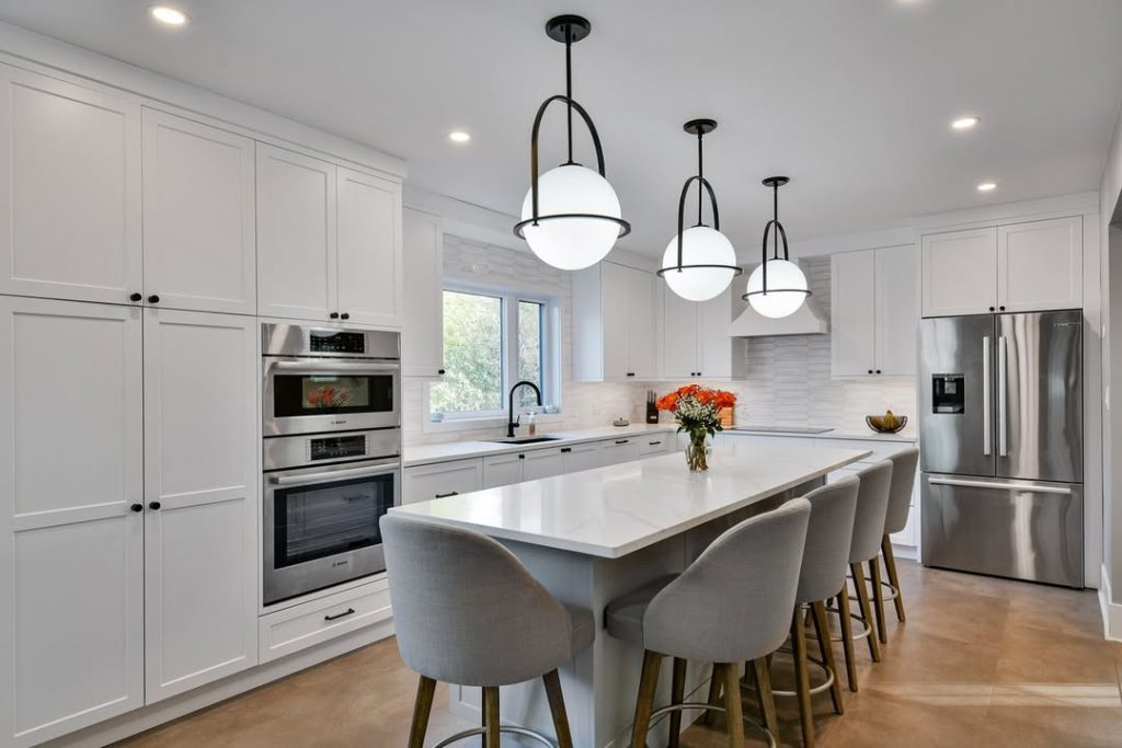 Modern kitchen with orb pendant lights, gray bar stools, white cabinets, linear backsplash