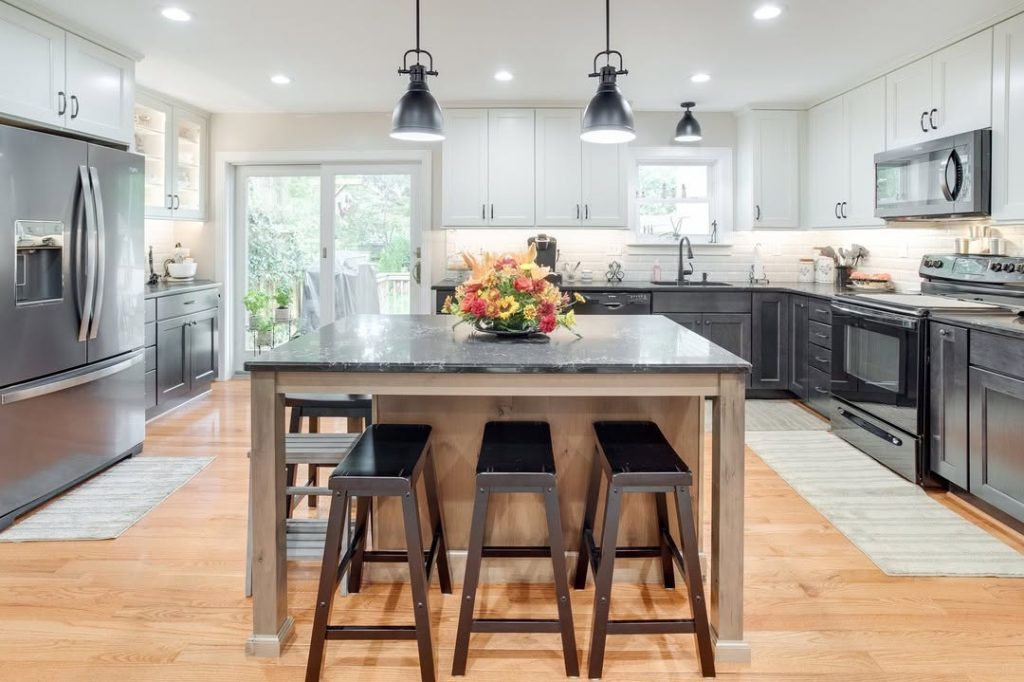 Industrial kitchen with black pendant lights, two-tone cabinets, wood island, metal bar stools
