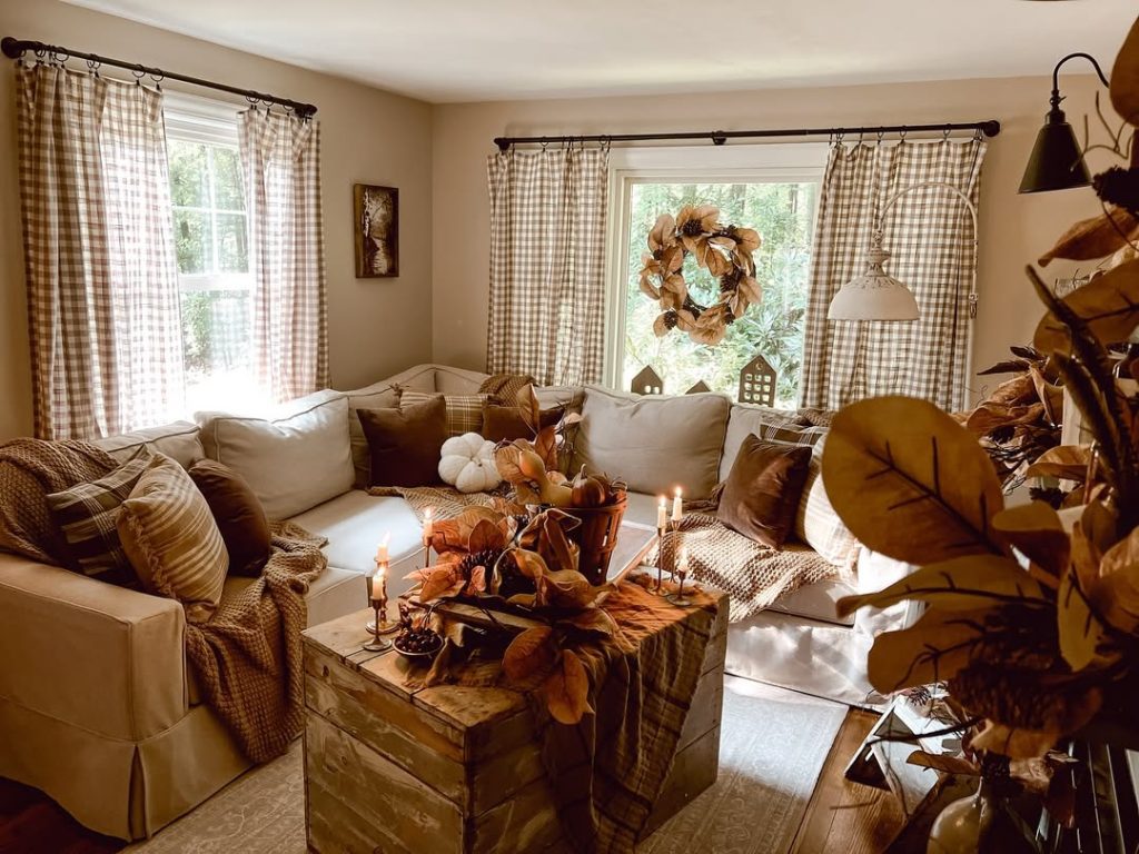 Cozy autumn living room with plaid curtains, pumpkin decorations, warm throws, and candlelit atmosphere
