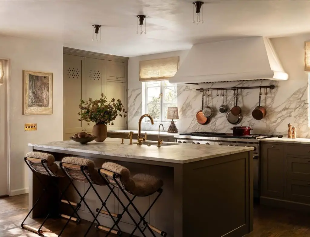 Green kitchen with marble backsplash, brass fixtures, woven stools