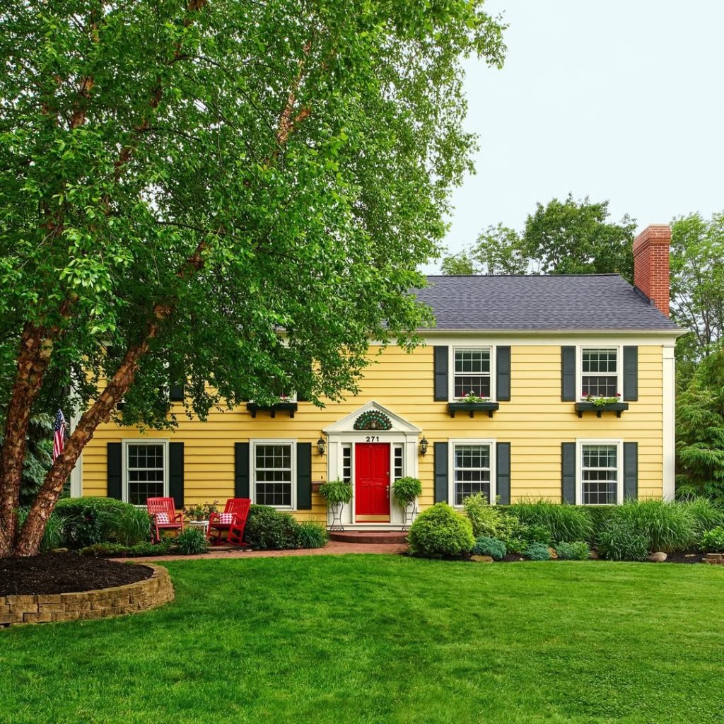 Yellow colonial house with green shutters red door