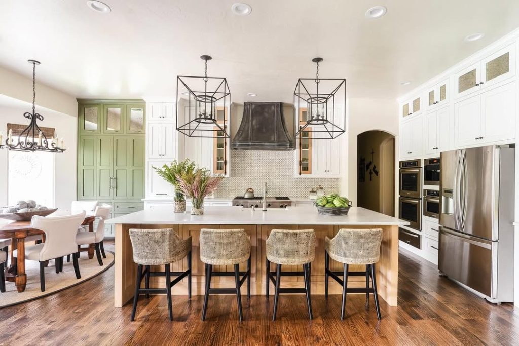 Kitchen with sage green cabinets, geometric pendant lights, wood bar stools, white countertops