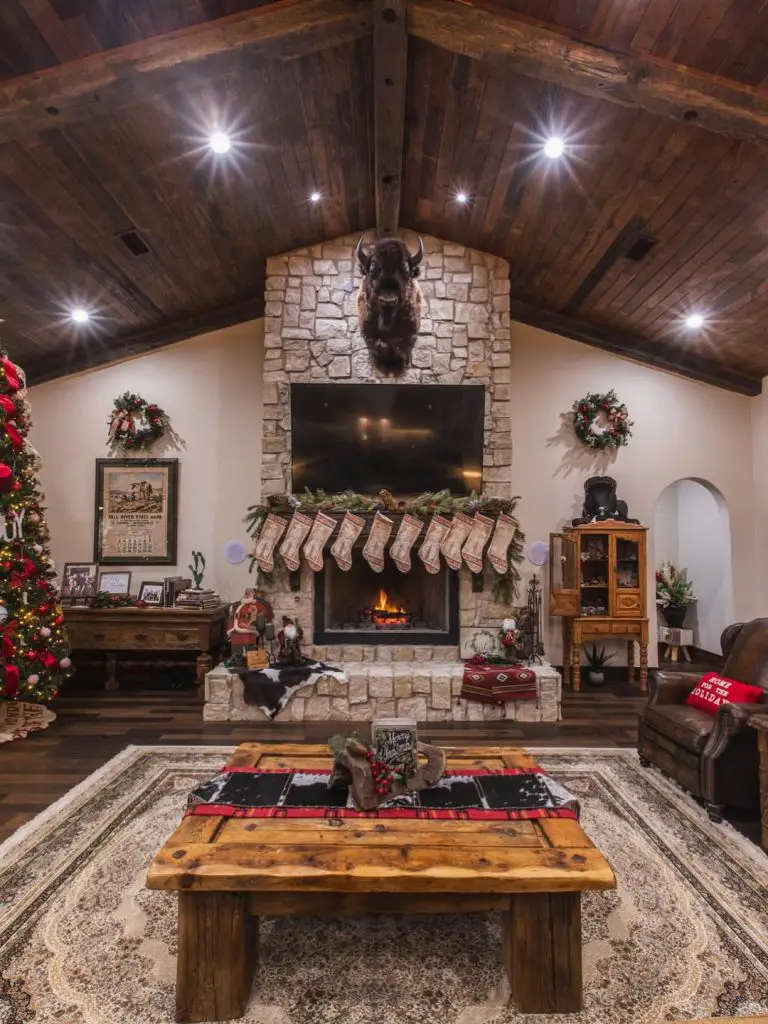 Rustic living room with stone fireplace, Christmas stockings, wooden beams, and holiday decorations.