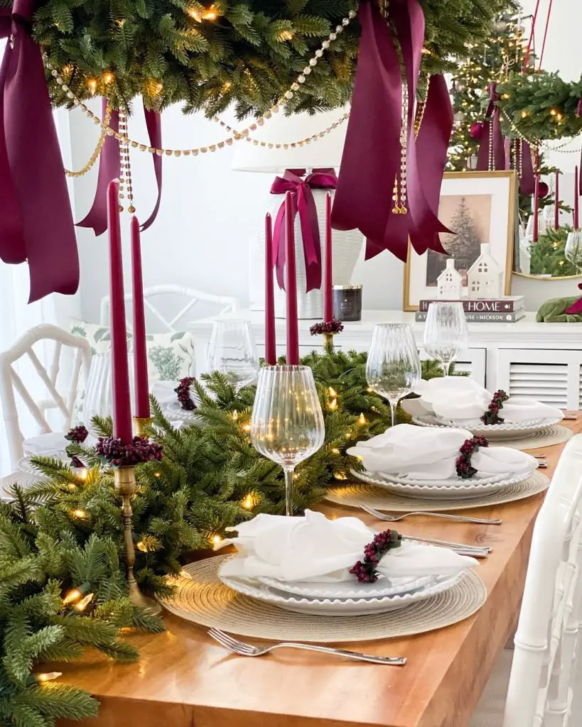 Elegant Christmas dining table with burgundy ribbons white plates evergreen garland