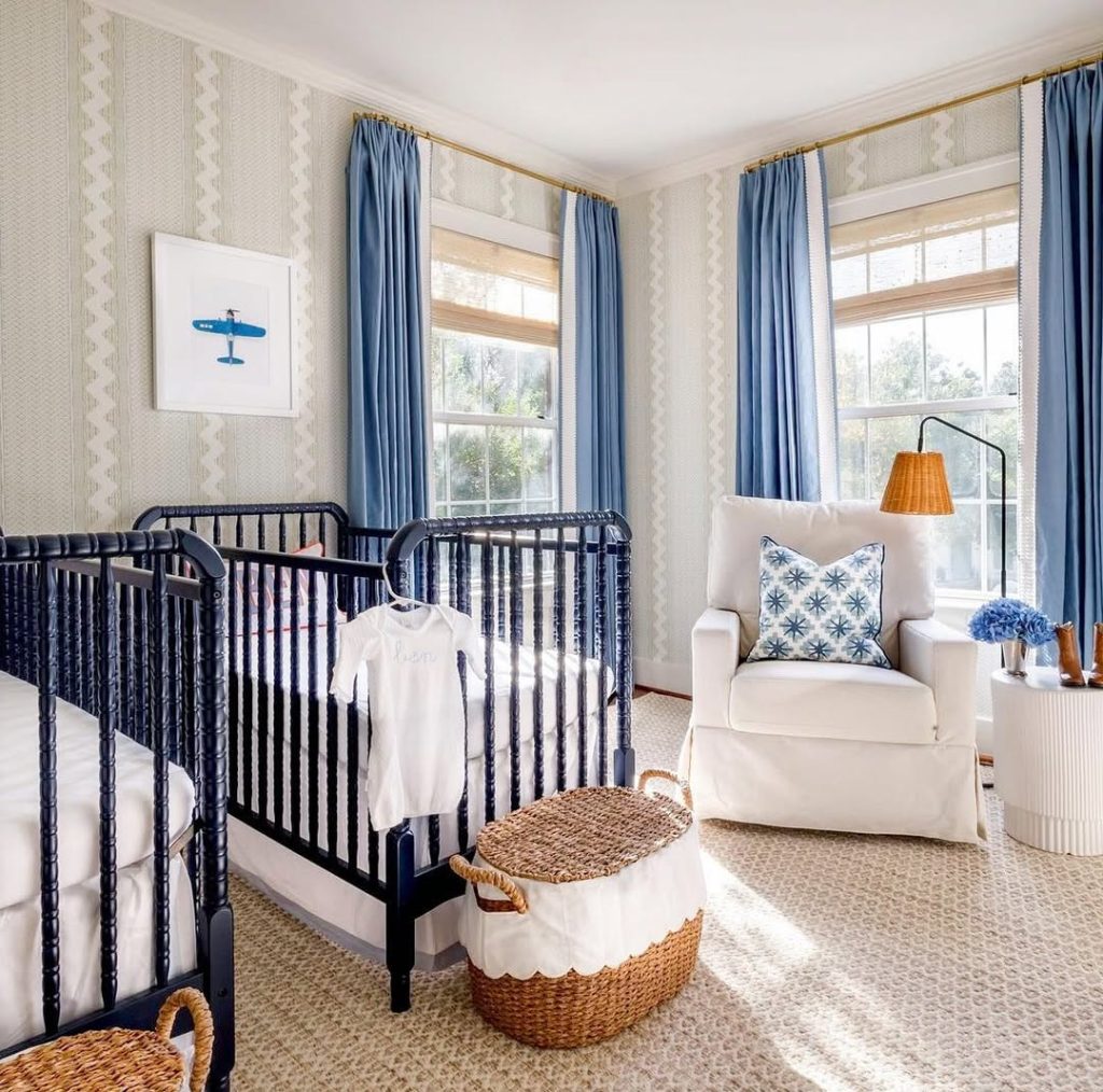 Navy blue nursery with twin cribs and comfortable seating chair.