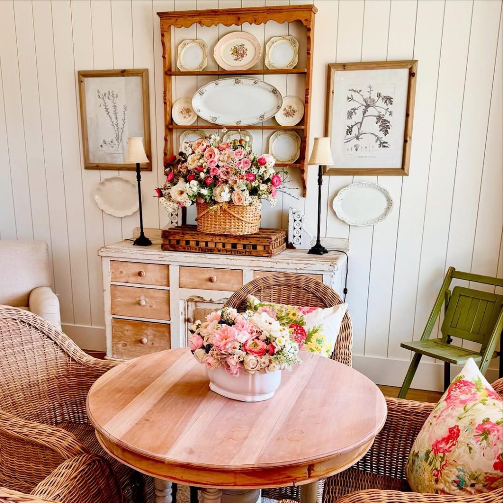 Country cottage room with vintage plates, wicker furniture, floral arrangements, botanical prints