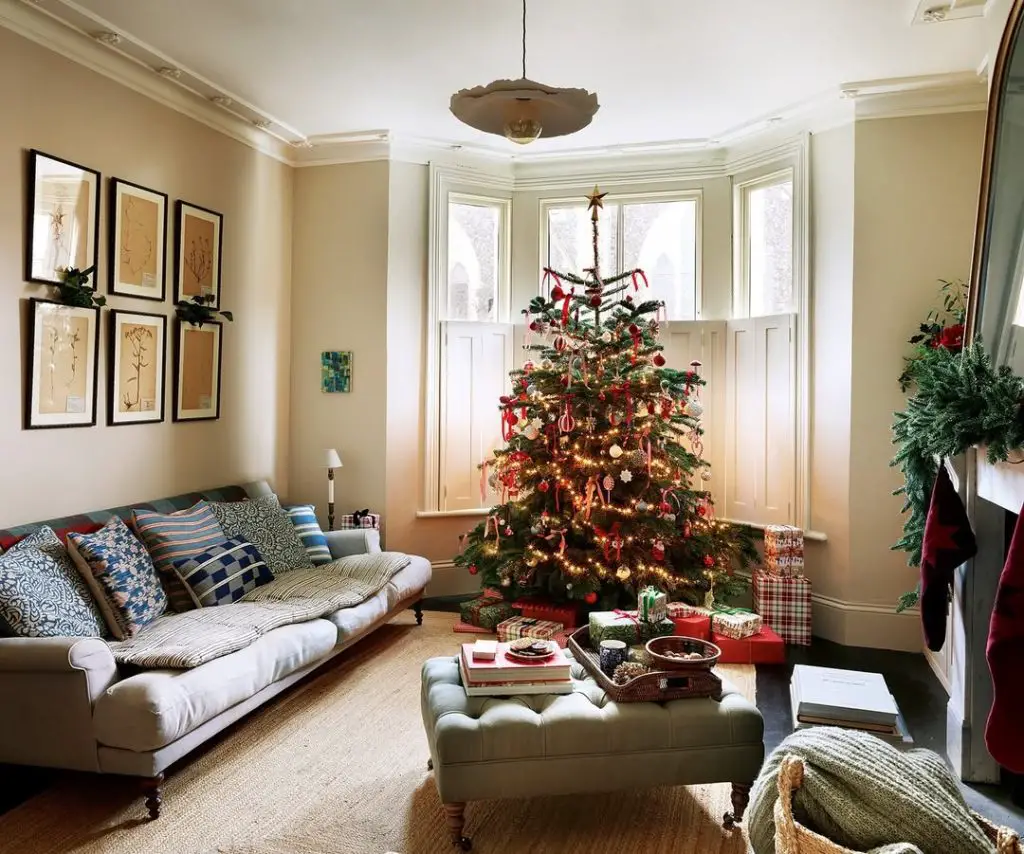 Christmas tree by bay window with neutral sofa and holiday decorations