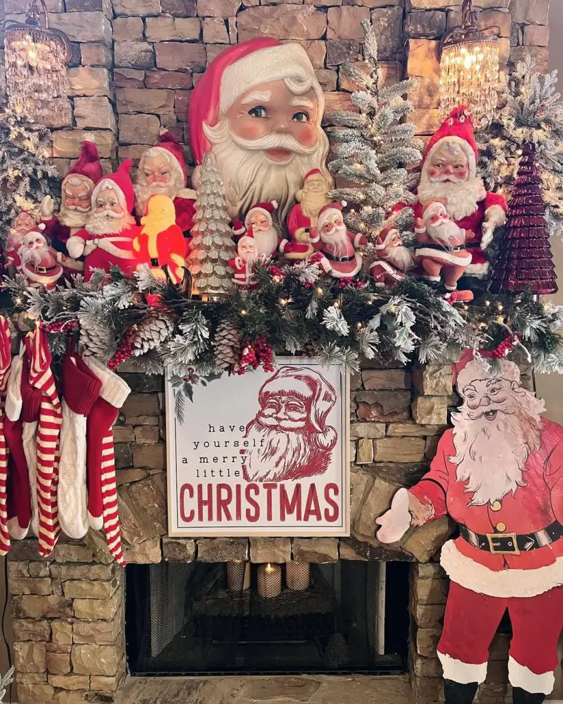 Stone fireplace mantel displaying vintage Santa collection, evergreen garland, holiday sign, warm lighting