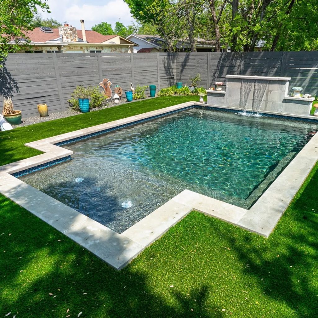 Rectangular backyard pool with waterfall feature and green lawn