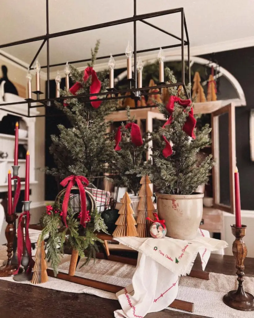 Black chandelier with candles, evergreen branches, red ribbons, rustic Christmas table setting