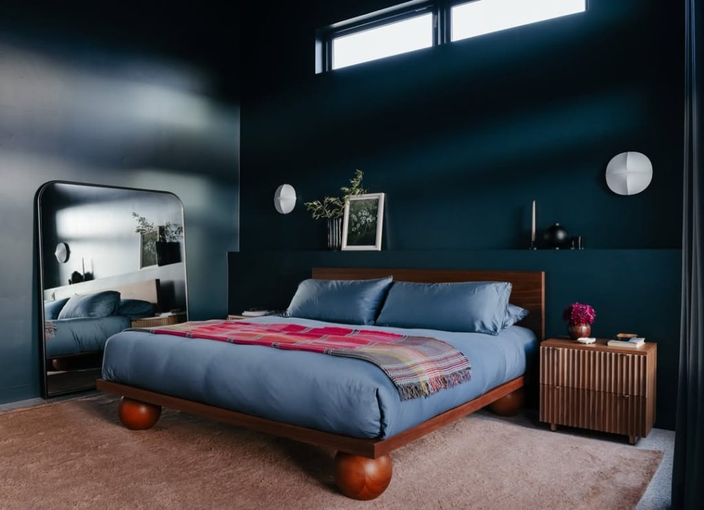 Navy bedroom with wood furniture and curved mirror