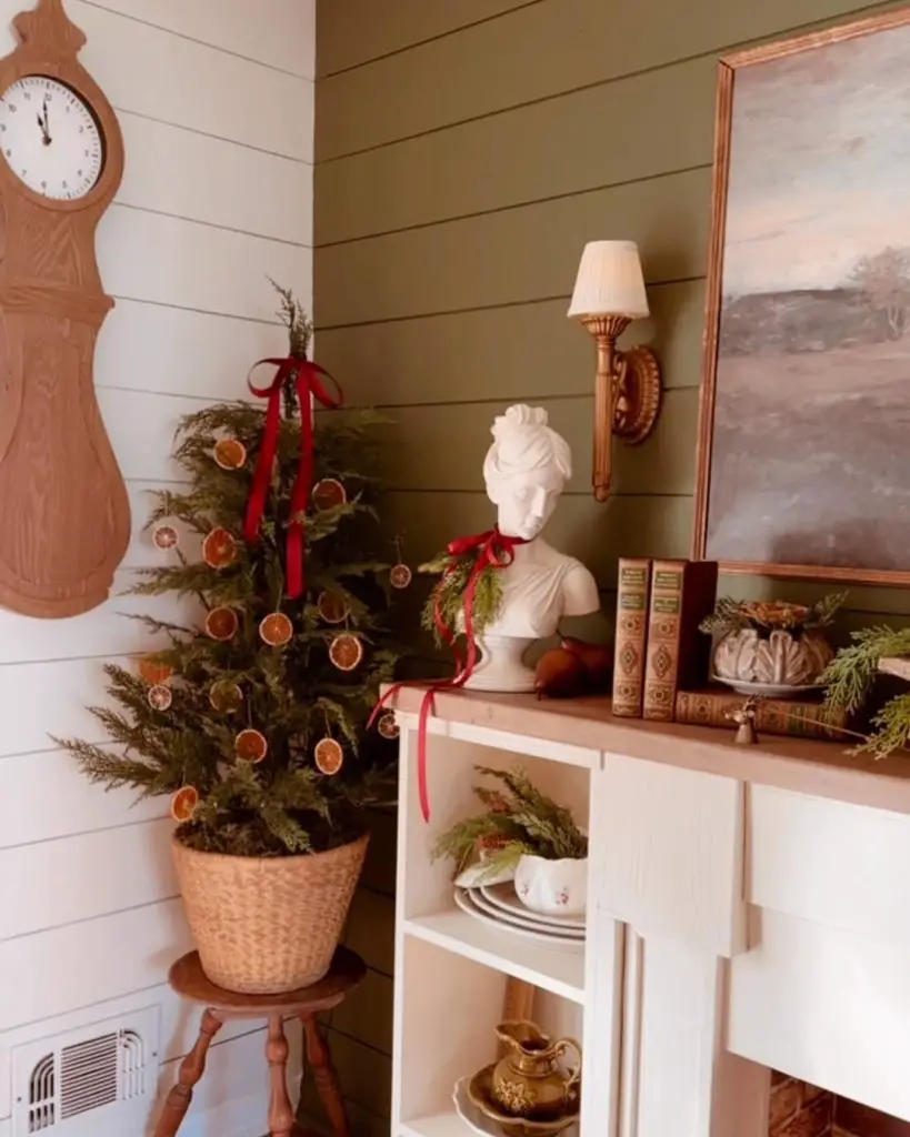 Holiday corner with small evergreen tree, dried oranges, wicker basket, classical bust, vintage books