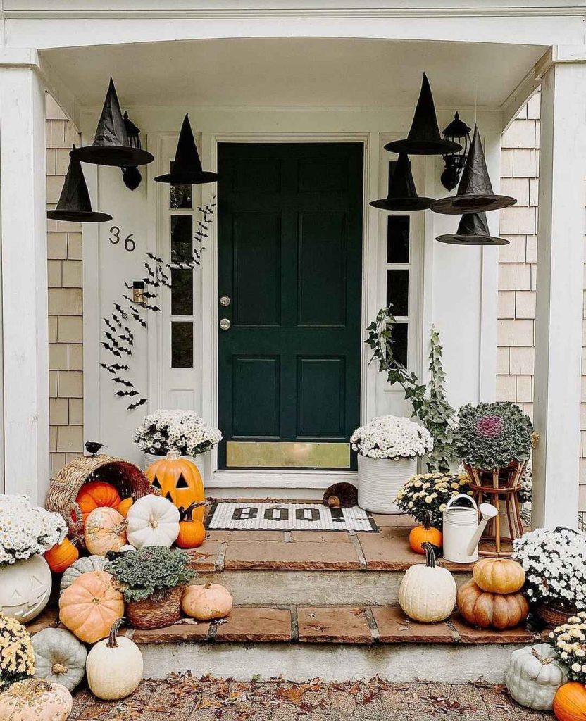 Green door entrance with hanging witch hats pumpkins autumn flowers steps