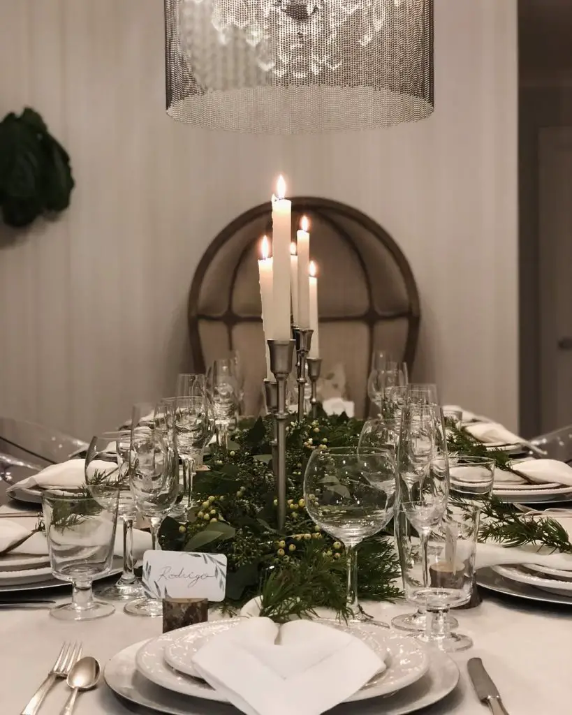 Elegant dining table with tall candles, evergreen centerpiece, and crystal glassware