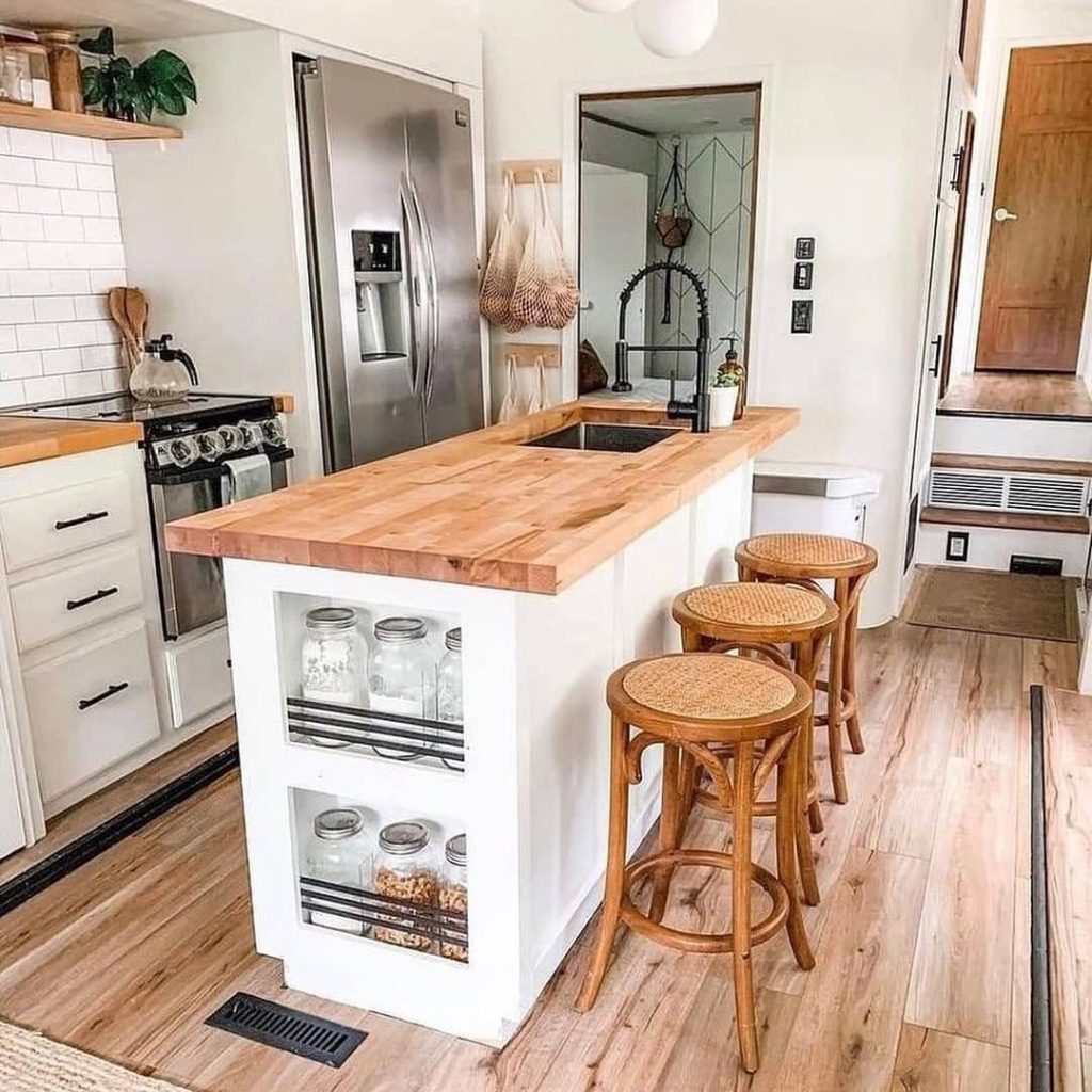 Kitchen island with wood countertop, white cabinets, woven stools, storage shelves