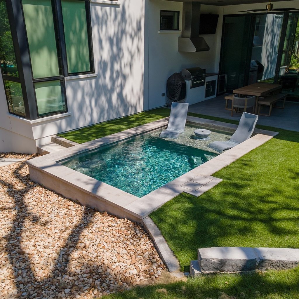 Modern pool with water features next to contemporary glass house