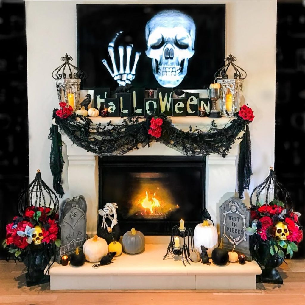 White fireplace with dramatic Halloween decorations including skull projection and gothic elements