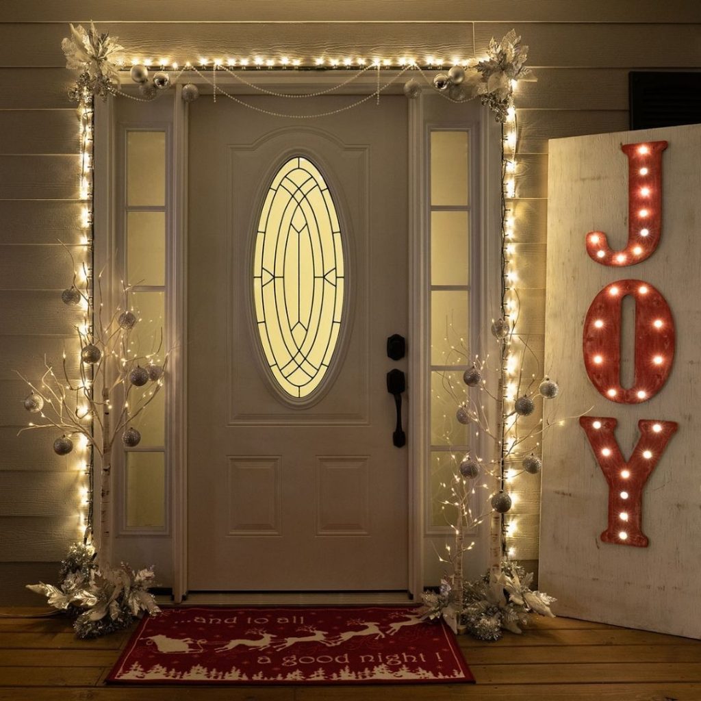 Front door with matching Christmas wreaths and illuminated potted trees