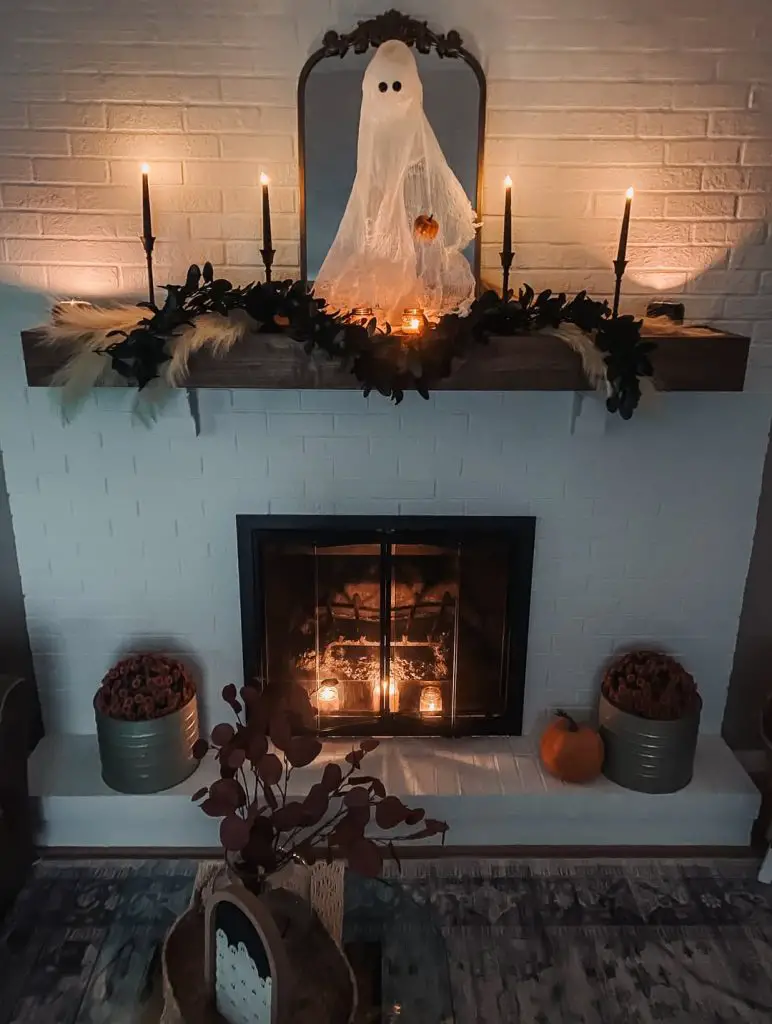 Brick fireplace with candlelit ghost display and dark garland creating atmospheric Halloween mood