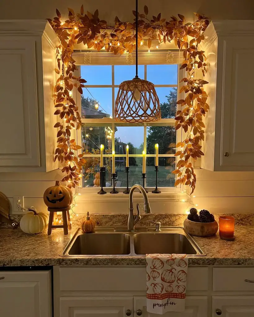 Kitchen window decorated with autumn leaf garland fairy lights pumpkins