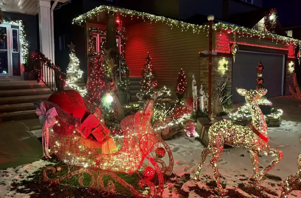 Illuminated wire reindeer in snow near stone house