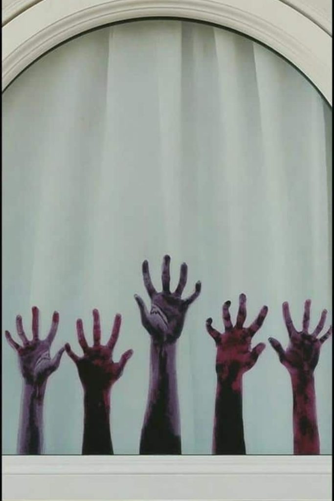 Zombie hands reaching upward on glass.